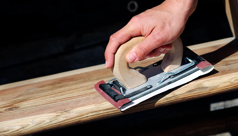 Abgenutzte Oberfläche einer Holzstufe wird mit dem Handschleifer bearbeitet